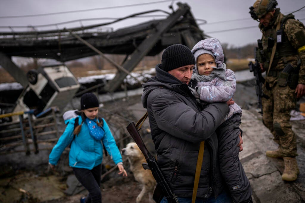 Valery carries a child as he helps a fleeing family across a bridge destroyed by artillery
