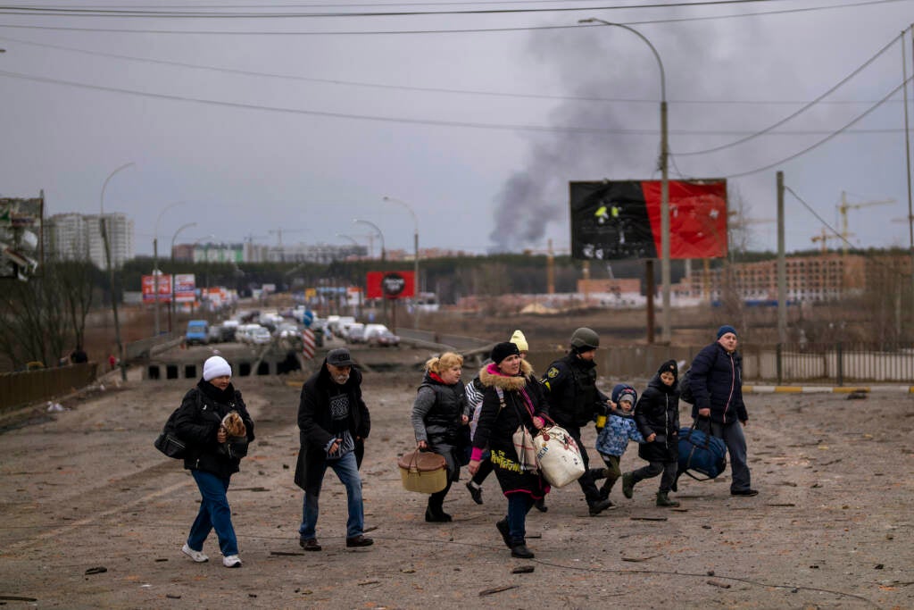 A Ukrainian police officer helps people as artillery echoes nearby while fleeing Irpin in the outskirts of Kyiv