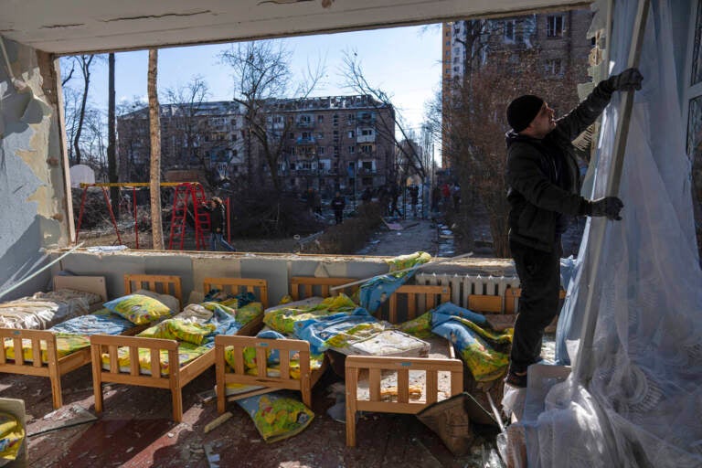 A man removes a destroyed curtain inside a school damaged among other residential buildings in Kyiv, Ukraine, Friday, March 18, 2022.