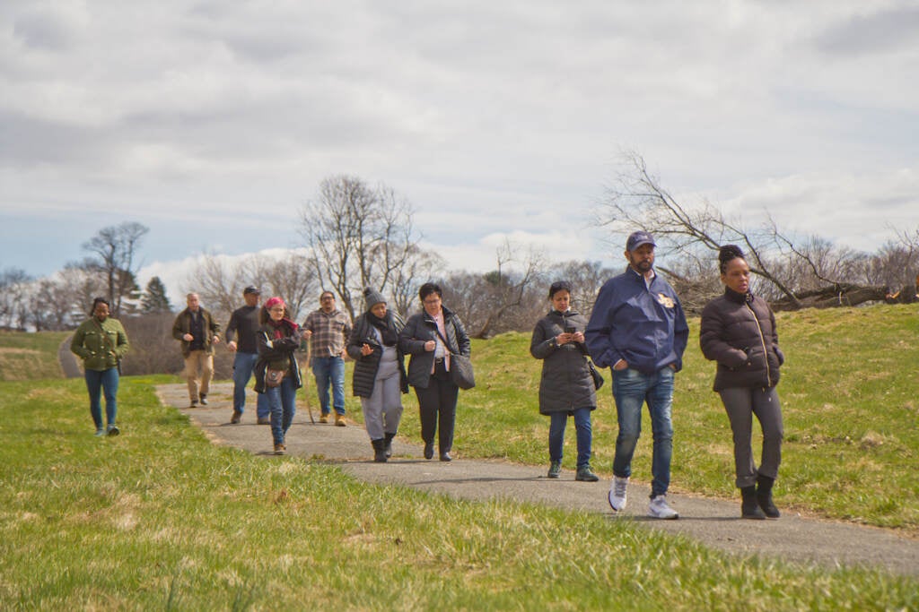 A group of people walk along a pavement path surrounded by green grass.