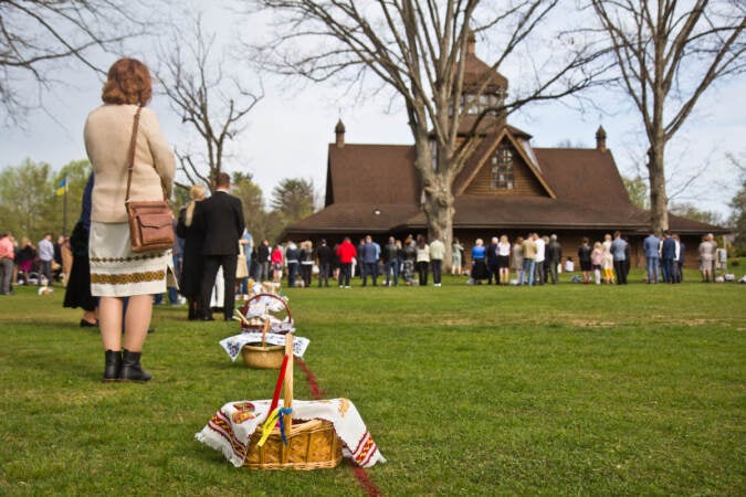 Parishioners face towards a wooden church in the background.