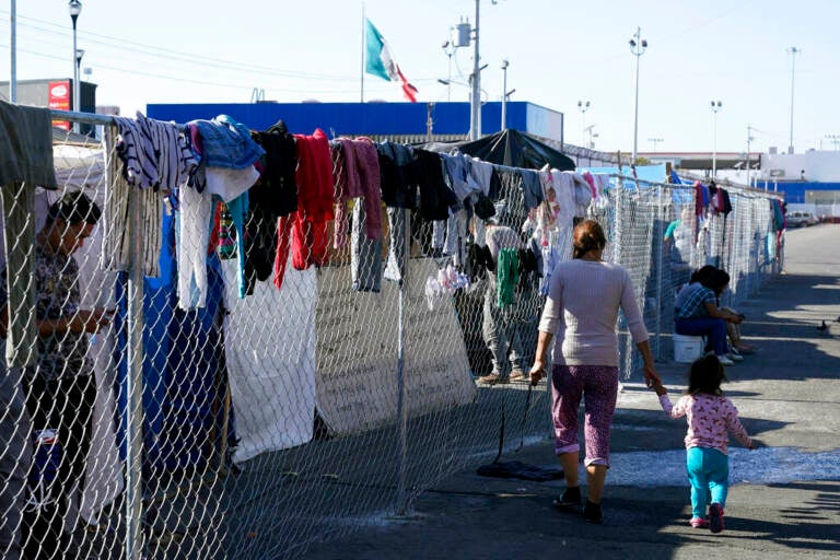 Migrants walk along a fence at a makeshift camp that is a temporary home for hundreds of migrants hoping to seek asylum in the United States at a pedestrian crossing on Nov. 8, 2021, in Tijuana, Mexico.