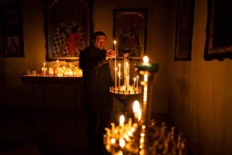 A man lights a candle during a Sunday service in an Orthodox church in Bucha, in the outskirts of Kyiv, Ukraine, Sunday, April 10, 2022.