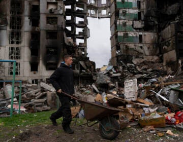 A young man pushes a wheelbarrow in front of a destroyed apartment building in the town of Borodyanka, Ukraine, on Sunday, April 10, 2022. Several apartment buildings were destroyed during fighting between the Russian troops and the Ukrainian forces and the town is without electricity, water and heating.