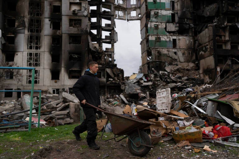 A young man pushes a wheelbarrow in front of a destroyed apartment building in the town of Borodyanka, Ukraine, on Sunday, April 10, 2022. Several apartment buildings were destroyed during fighting between the Russian troops and the Ukrainian forces and the town is without electricity, water and heating.