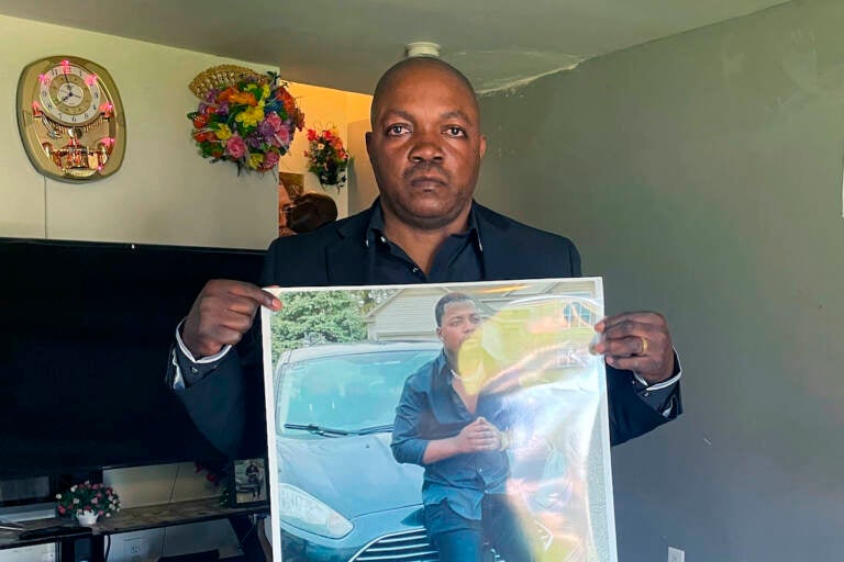 Peter Lyoya holds up a picture of his son Patrick Lyoya, 26, in his home in Lansing, Mich., April 14, 2022. Patrick was face-down on the ground when he was fatally shot in the head by a Grand Rapids Police officer after resisting arrest on April 4, 2022. Grand Rapids police released four videos from different sources Wednesday, nine days after Patrick Lyoya was killed during a traffic stop. Prominent civil rights attorney Ben Crump and Lyoya's family are planning to hold a news conference Thursday afternoon