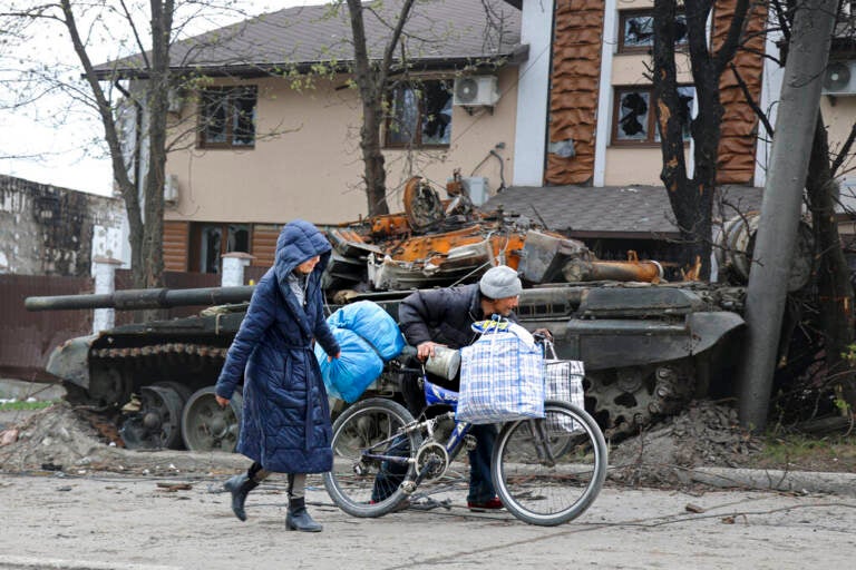 Local civilians walk past a tank destroyed during heavy fighting in Mariupol