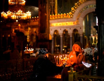 A woman lights candles in a darkened church.