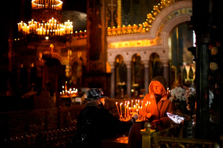 A woman lights candles in a darkened church.