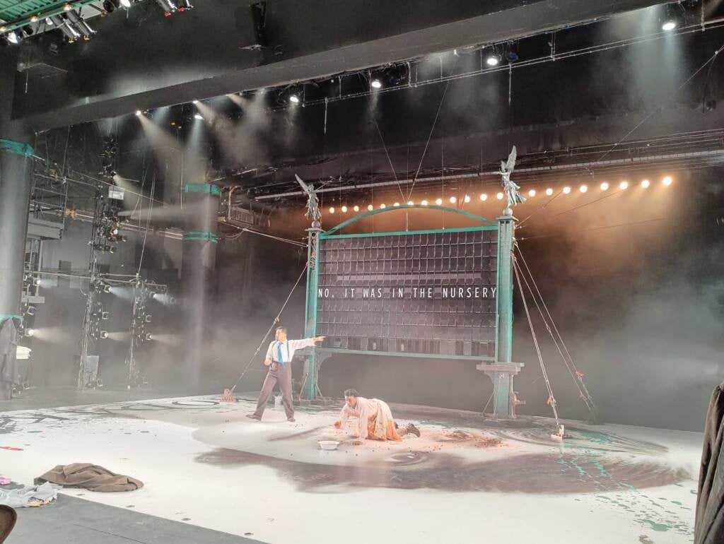 Brett Ashley Robinson tries to clean up spilled cherries as Justin Jain interacts with a sentient split flap train station sign in the Wilma Theater's production of Anton Chekhov's "The Cherry Orchard."