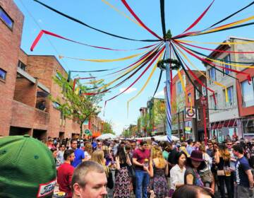 A maypole is visible above a crowd of people walking through the street.