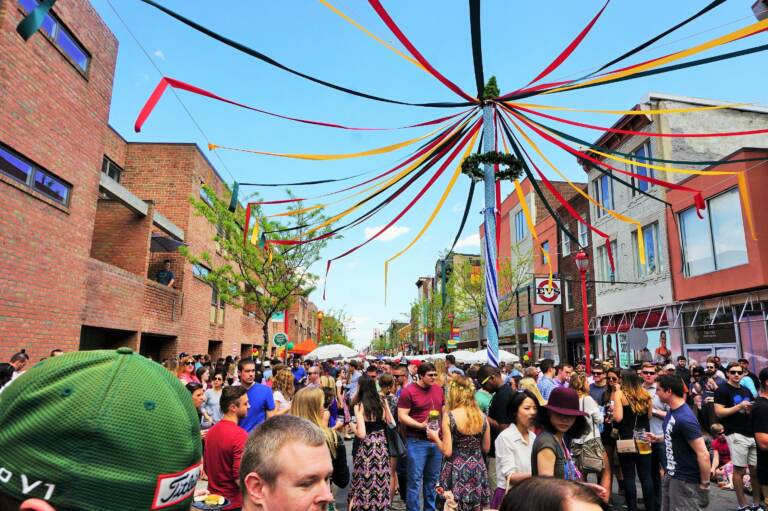 A maypole is visible above a crowd of people walking through the street.