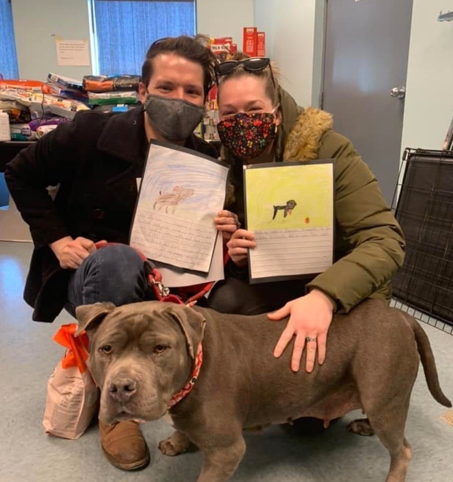 Two people wearing face masks pose with a dog they adopted at RACC