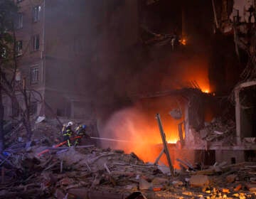 Bright flames are visible in a building that is partially destroyed.