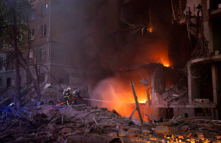 Bright flames are visible in a building that is partially destroyed.