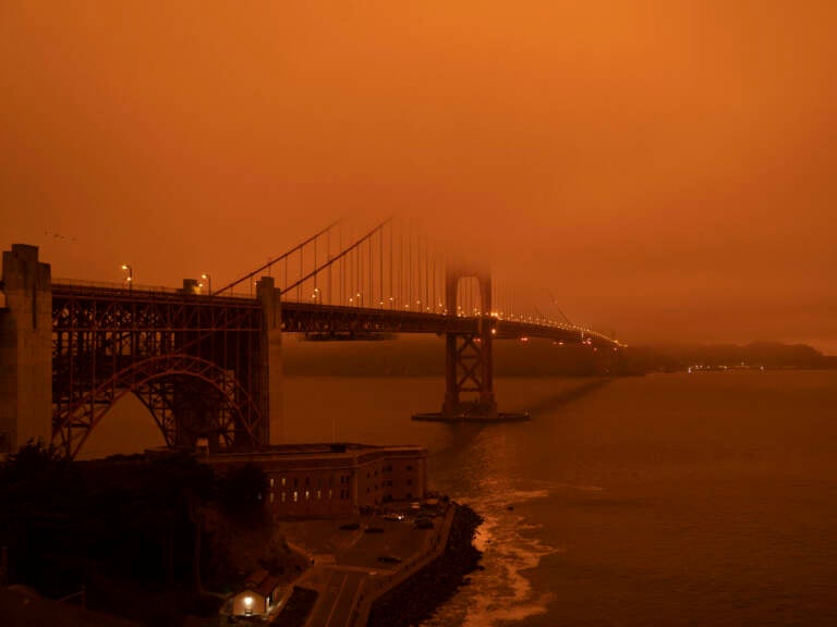 Cars drive along the Golden Gate Bridge under an orange smoke-filled sky