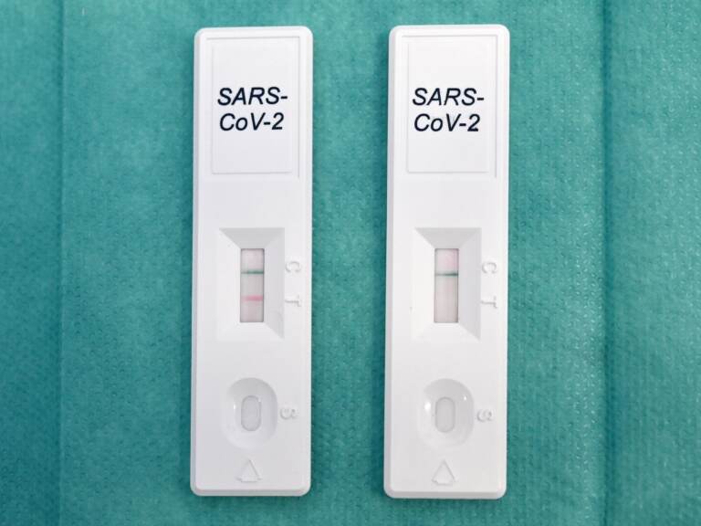 Two COVID tests are shown on a teal background.