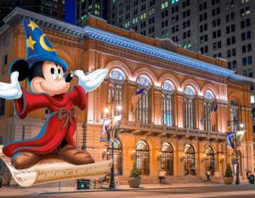 An image of Mickey Mouse in the foreground with the Academy of Music on South Broad Street in the background.