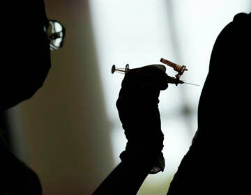 A silhouette of a health worker administering a COVID-19 vaccine