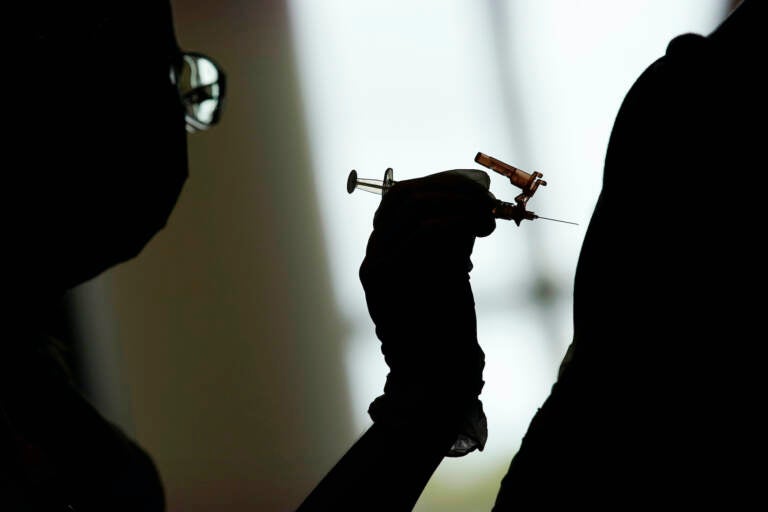 A silhouette of a health worker administering a COVID-19 vaccine