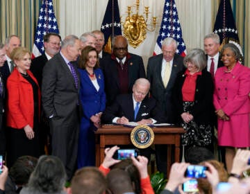 President Joe Biden signs the Postal Service Reform Act of 2022 in the State Dining Room, surrounded by elected officials