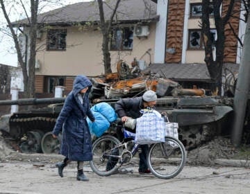 Local civilians walk past a tank destroyed during heavy fighting in Mariupol