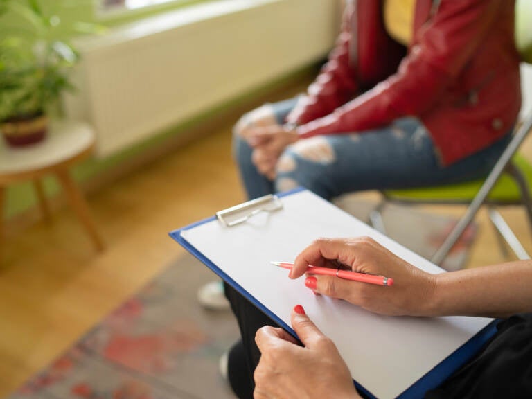 Close up of a psychologist notes and a student's knees during a mental health meeting