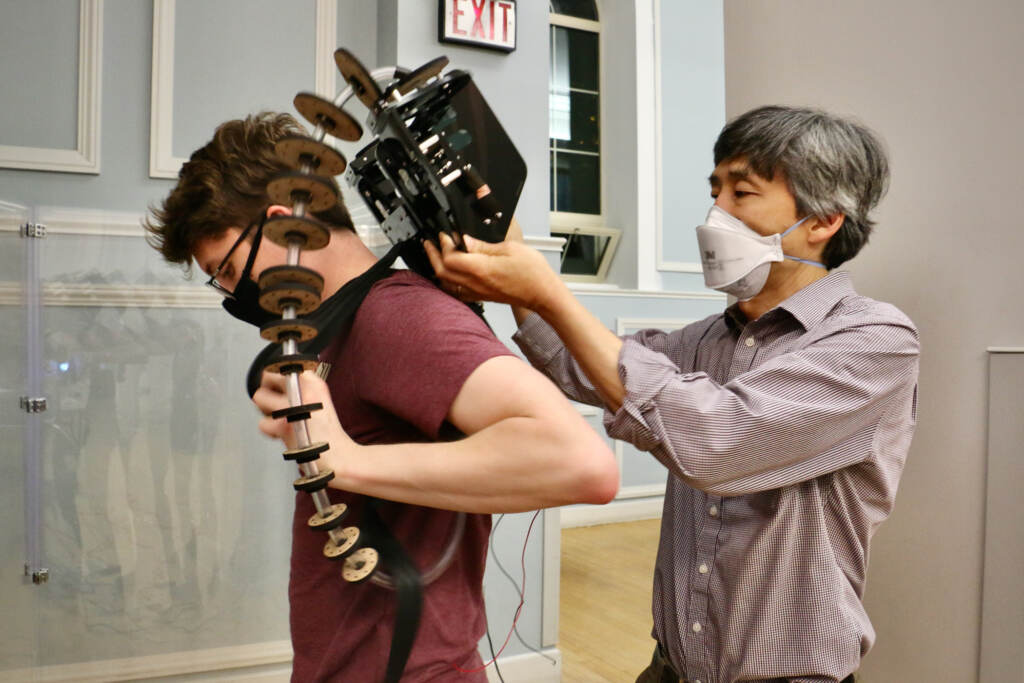 Mark Yim (right), director of the University of Pennsylvania's GRASP Lab, helps student Evan Grant put on a robotic costume designed at the lab.