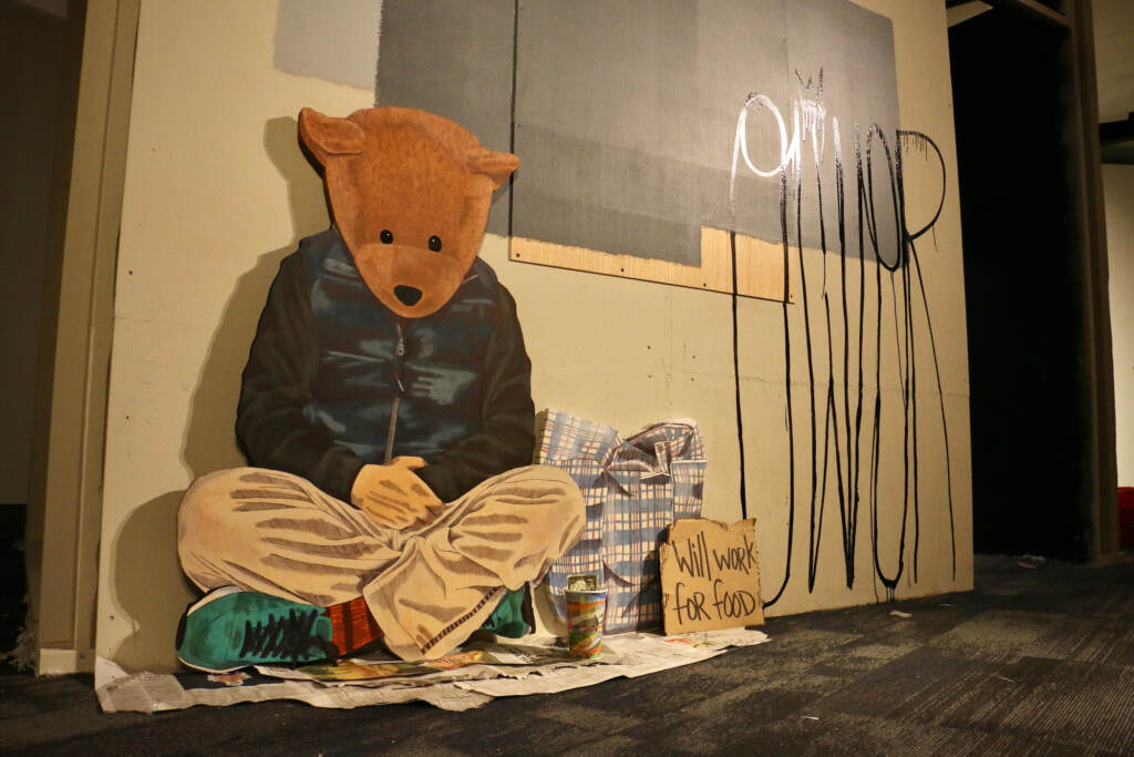 An art exhibition, consisting of a cutout of a bear asking for help, is visible.