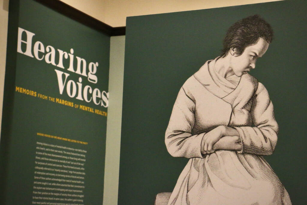 The exhibition information for Hearing Voices is displayed alongside an image of a person clutching their hands to their body, with eyes downcast.