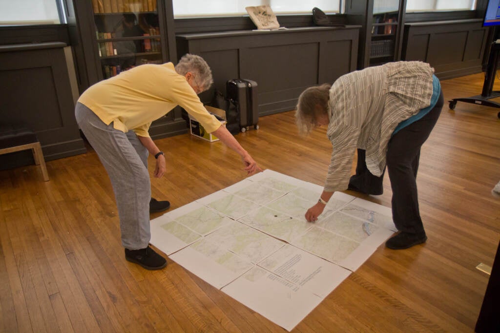 Two artists bend over a map, pointing at different parts of it.