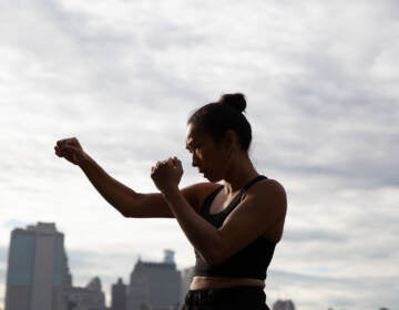 Jess Ng is shown in a defensive stance, with city buildings and sky behind her.