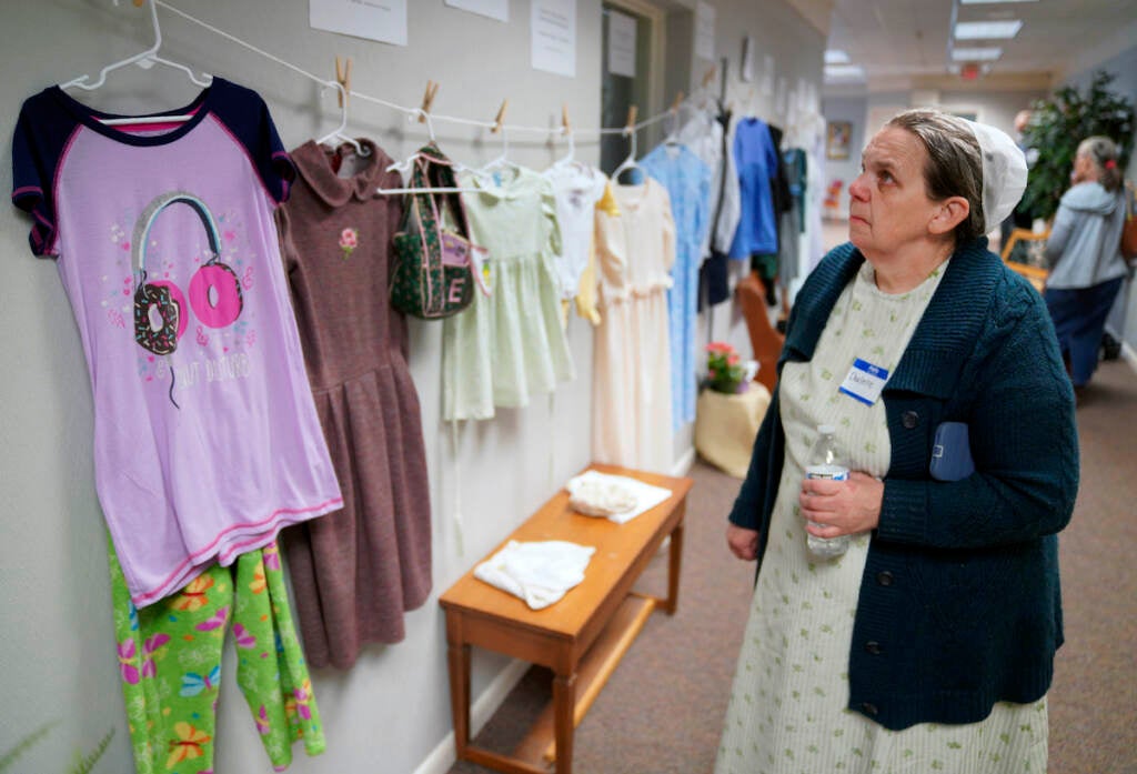 Darlene Shirk looks at the clothes of sexual assault survivors from Amish, Mennonite and other plain-dressing religious groups on display at a child abuse prevention seminar, on Friday, April 29, 2022, in Leola, Pa. Some plain-dressing traditions allow for modern nightwear. Similar exhibits held nationwide aim to shatter the myth that abuse is caused by a victim's clothing choice.