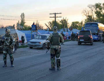 Servicemen of Russian Army and Donetsk People's Republic militia guard the camp where local residents who left a shelter in the Metallurgical Combine Azovstal temporary staying in Bezimenne, in territory under the government of the Donetsk People's Republic, eastern Ukraine, Friday, May 6, 2022. (AP Photo/Alexei Alexandrov)