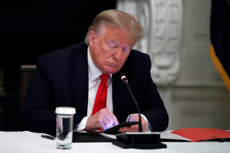 File photo: President Donald Trump looks at his phone during a roundtable with governors on the reopening of America's small businesses, in the State Dining Room of the White House in Washington, June 18, 2020. (AP Photo/Alex Brandon, File)