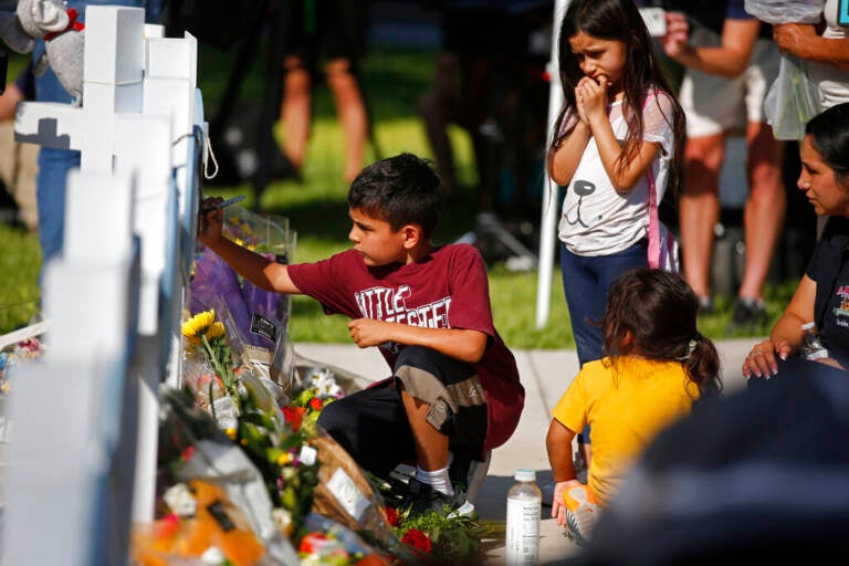 A child writes a message on a cross at a memorial site for the victims killed in this week's elementary school shooting in Uvalde, Texas, Thursday, May 26, 2022. (AP Photo/Dario Lopez-Mills)