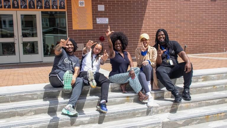 Marla Travis, center, on the steps of West Philadelphia High School, where she is the principal, with four of her former students at Lamberton High who are now teachers at West Philadelphia. From left: Jean-Claude Forte, Yaseemah Foster, Brittney Smith, and Robert Green. They are flashing the “L” Lamberton sign. (Tyriq Williams, student, West Philadelphia High School)