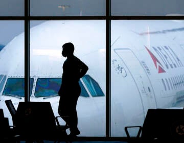 A silhouette of a person standing in an airport is visible, with a plane visible in the background, outside the window.