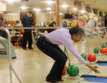 A person bends down as they release a bowling ball from their hand.