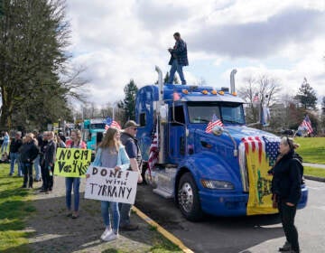 People hold signs as they stand near parked semi-trucks during a protest against COVID-19 vaccine mandates