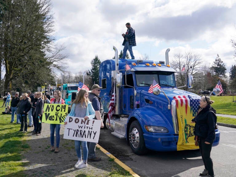 People hold signs as they stand near parked semi-trucks during a protest against COVID-19 vaccine mandates