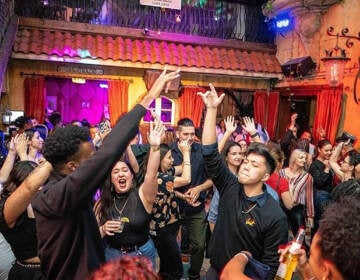 People are dancing with their arms up, and colorful lights in the background.