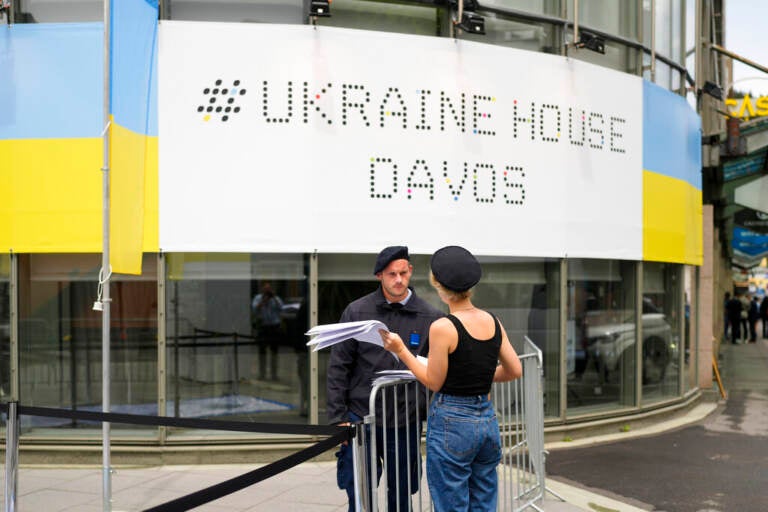 A security guard talks to a women in front of the Ukrainian House alongside the World Economy Forum in Davos, Switzerland, Sunday, May 22, 2022. The annual meeting of the World Economy Forum is taking place in Davos from May. 22 until May. 26, 2020.