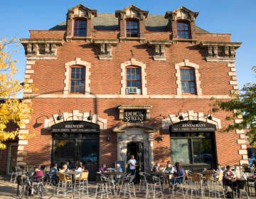 The brick building which currently houses Dock Street Brewing in West Philly is visible in the early evening sunlight. People are sitting at tables outside.