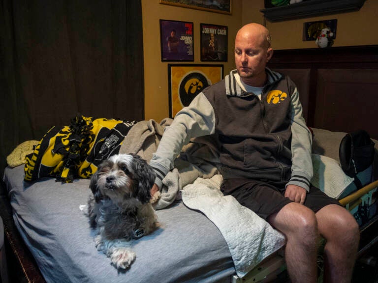 Jon Miller sits in his bedroom with his dog, Carlos, whom he received as a present for successfully completing cancer treatment a decade ago.
