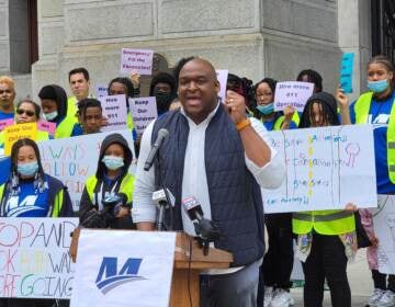 LeYondo Dunn speaks from a podium with protesters behind him