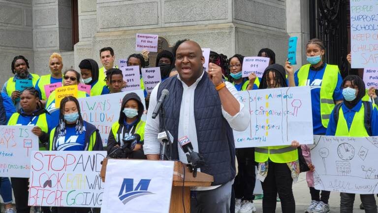 LeYondo Dunn speaks from a podium with protesters behind him