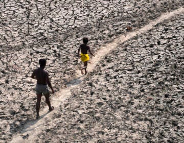 FILE - A man and a boy walk across the almost dried up bed of river Yamuna following hot weather in New Delhi, India, Monday, May 2, 2022. According to a report released by the World Meteorological Organization on Monday, May 9, 2022, the world is creeping closer to the warming threshold international agreements are trying to prevent, with nearly a 50-50 chance that Earth will temporarily hit that temperature mark within the next five years. (AP Photo/Manish Swarup, File)