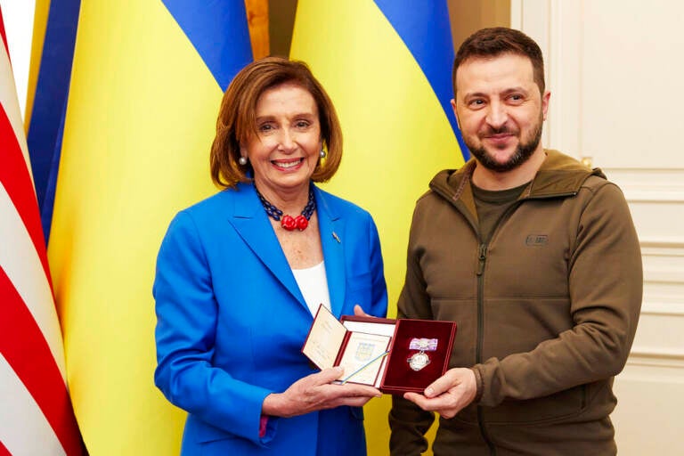 Nancy Pelosi stands next to Volodymyr Zelenskyy, both are smiling.