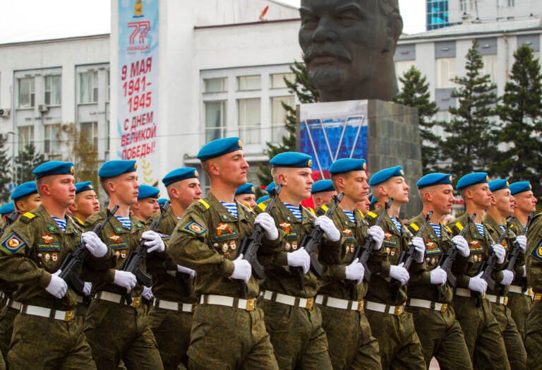 Russian soldiers march in one line, with a statue in the background.